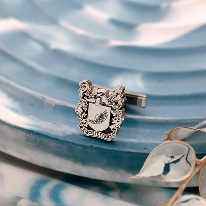 Silver crest-shaped cufflinks with 'Hostetter' on a blue textured background