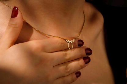Gold necklace with a bow pendant held by hands with red nail polish.