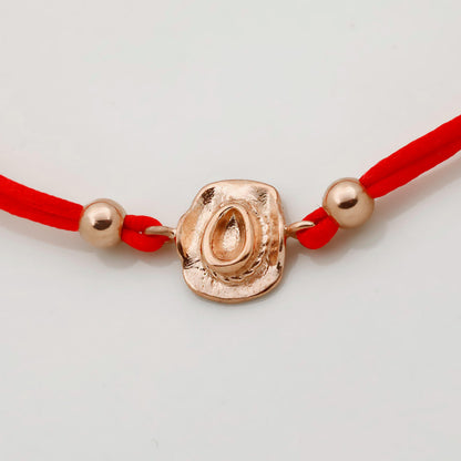Bracelet with red cord and gold clasp on a light gray background