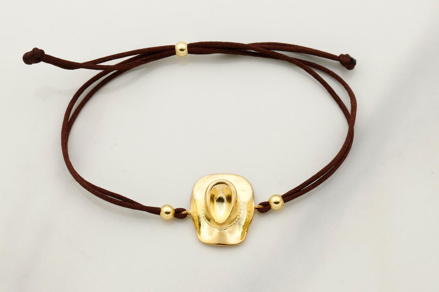 Gold bracelet with a brown cord on a light gray background