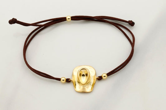 Gold bracelet with a brown cord on a light gray background