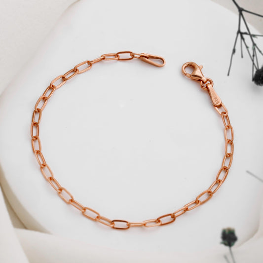 Rose gold chain bracelet on a white surface with a blurred background