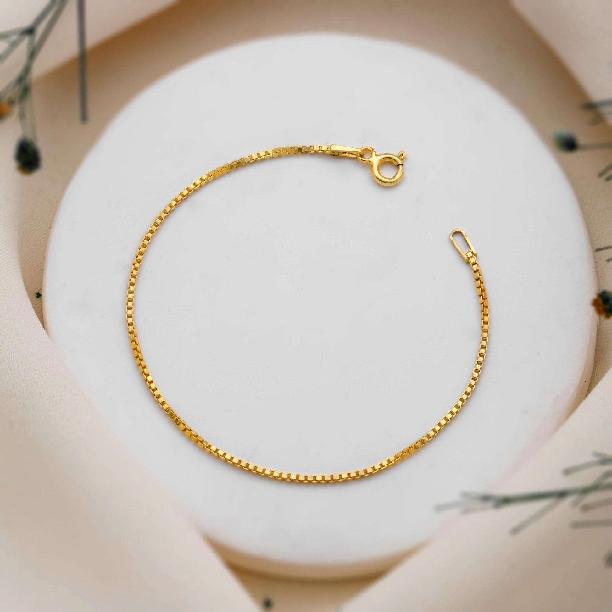 Gold chain bracelet on a white surface with a blurred natural background