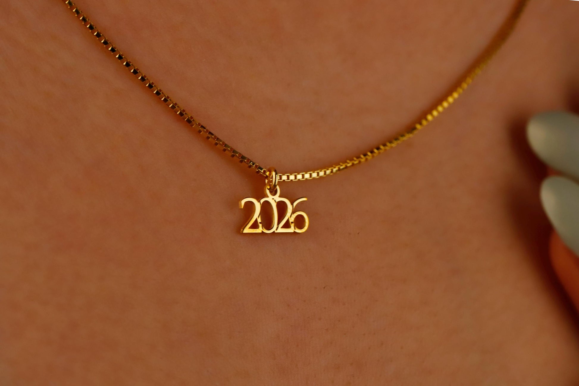 Gold necklace with '2026' pendant on a blurred background