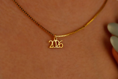 Gold necklace with '2026' pendant on a blurred background