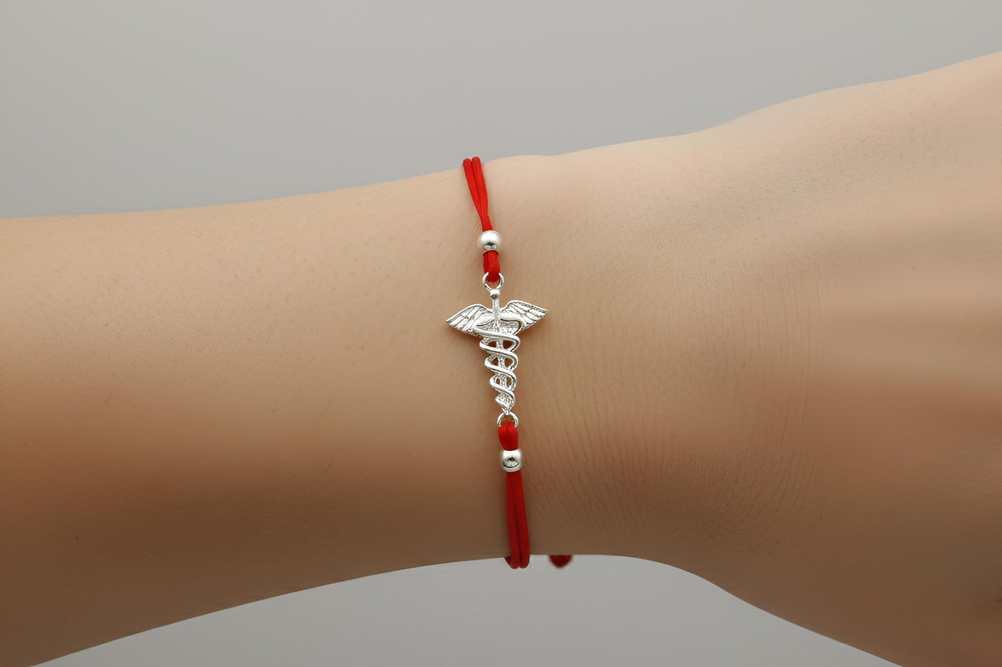 Red bracelet with a silver medical symbol on a wrist against a gray background