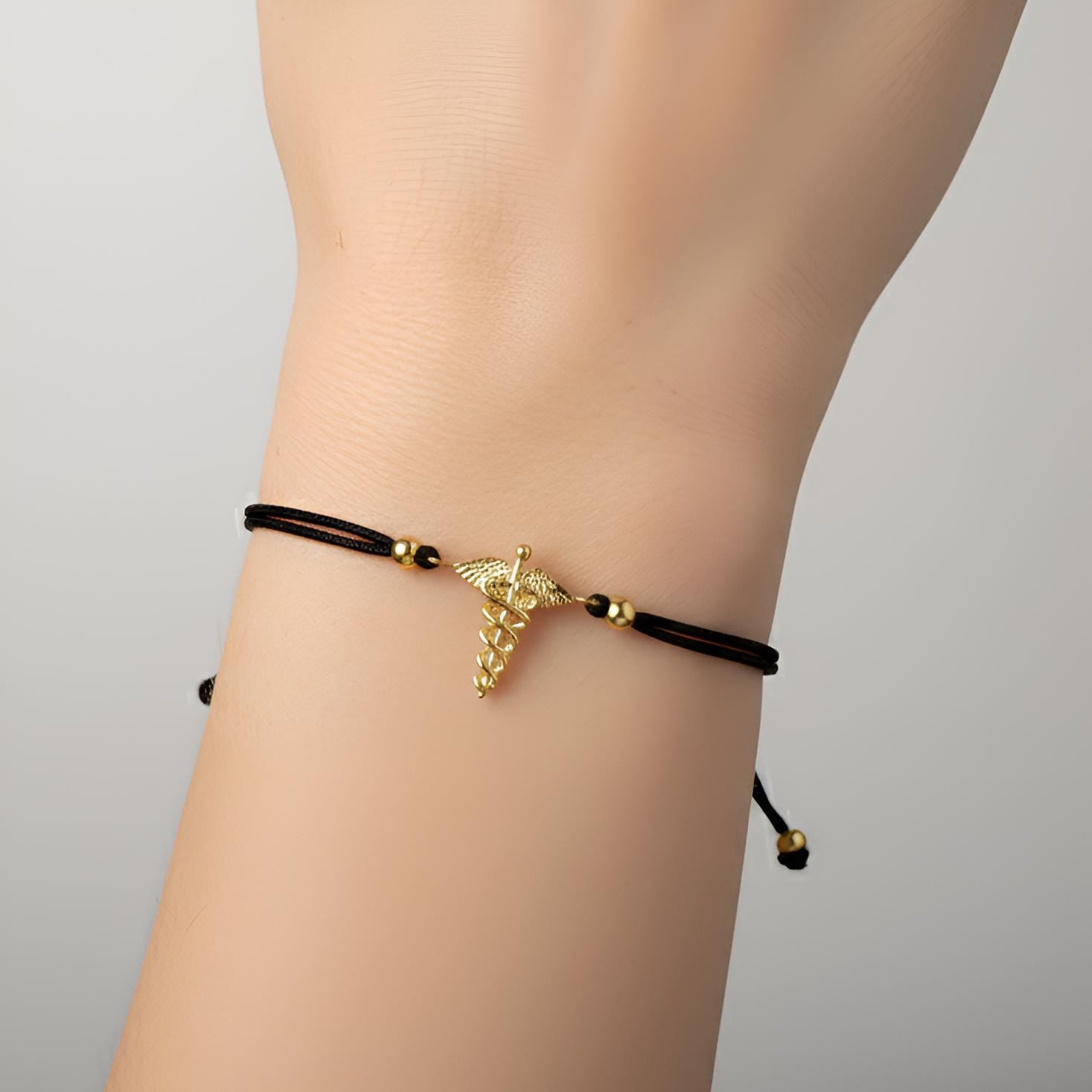 Black bracelet with a gold feather charm on a wrist against a gray background