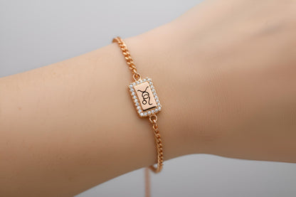 Rose gold bracelet with a rectangular charm on a wrist against a neutral background