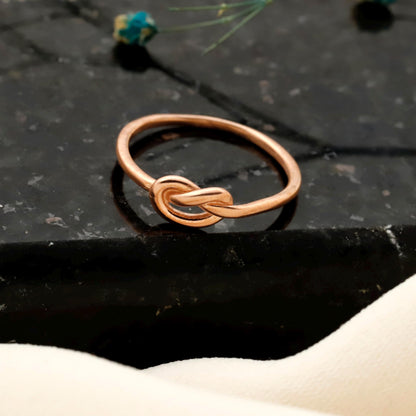 Rose gold knot ring on a dark stone surface