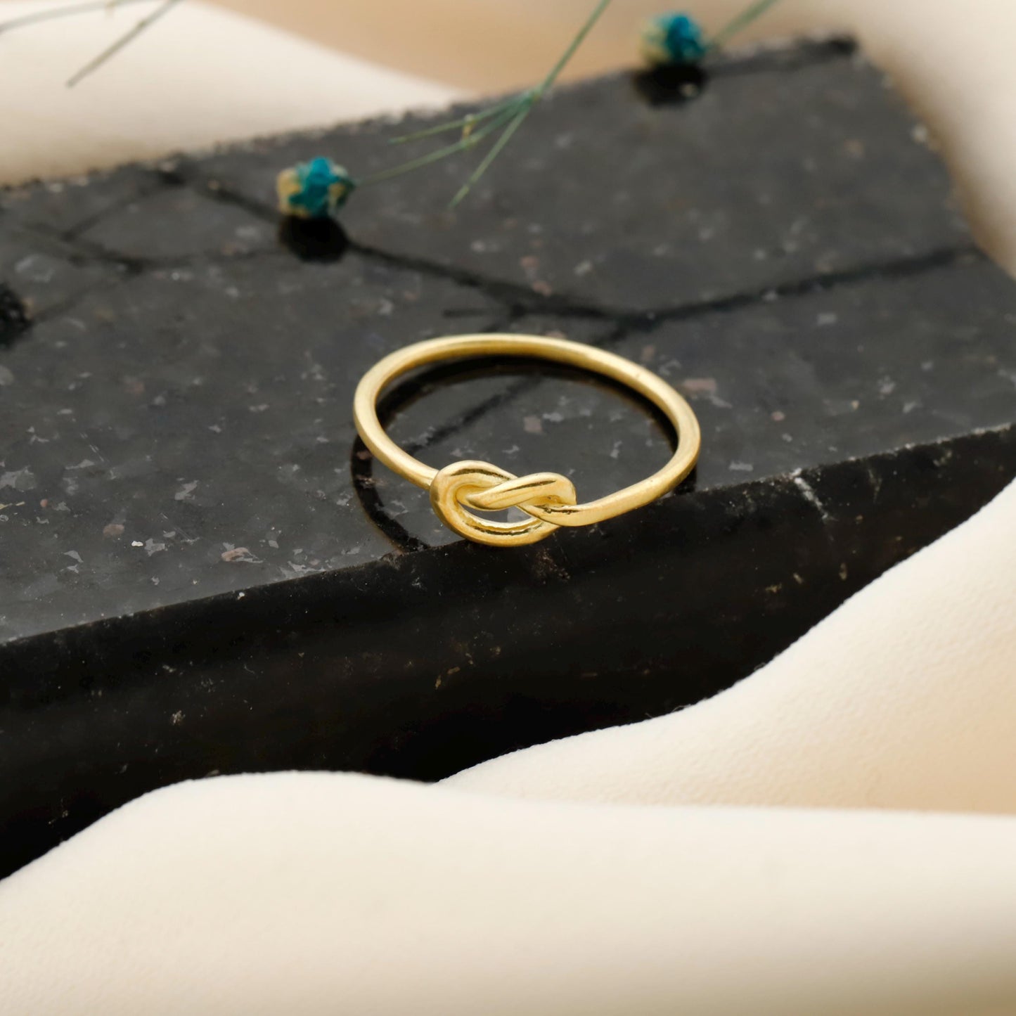 Gold ring with a knot design on a black stone surface