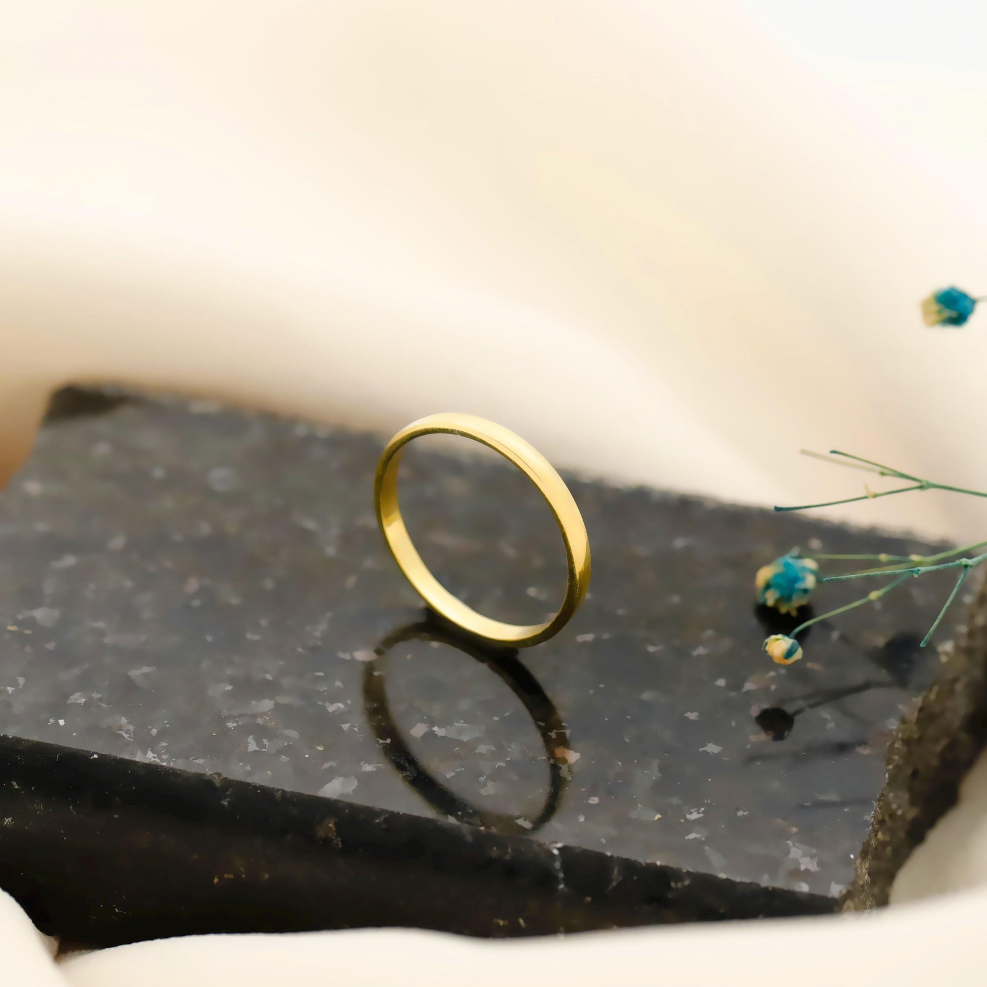 Gold ring on a dark stone surface with small flowers