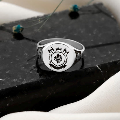 Silver ring with a black emblem on a dark surface