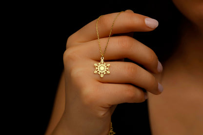 Hand holding a gold necklace with a snowflake pendant against a dark background