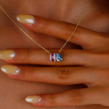 Gold necklace with a pink and blue gemstone pendant on a hand.
