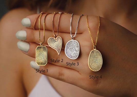 Four gold fingerprint pendants on a hand with blurred background