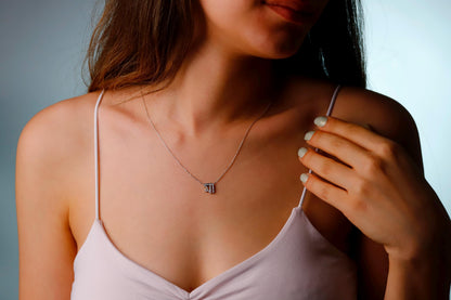Woman wearing a delicate necklace with a small pendant against a neutral background