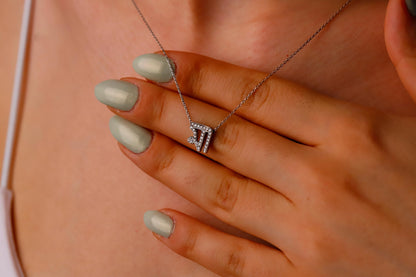 Close-up of a hand wearing a silver necklace with a zodiac pendant on a neutral background