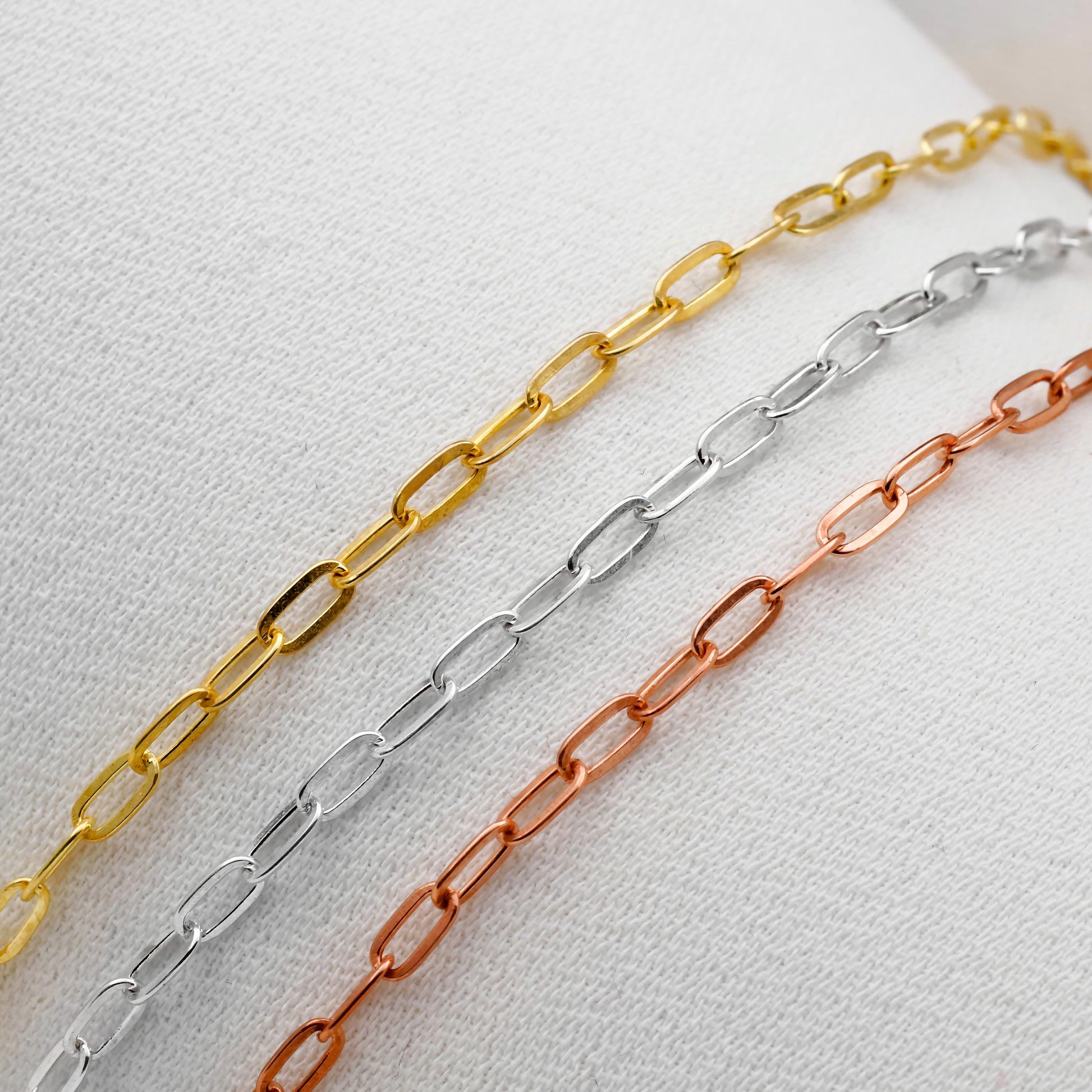 Three chain necklaces in gold, silver, and rose gold on a light gray background