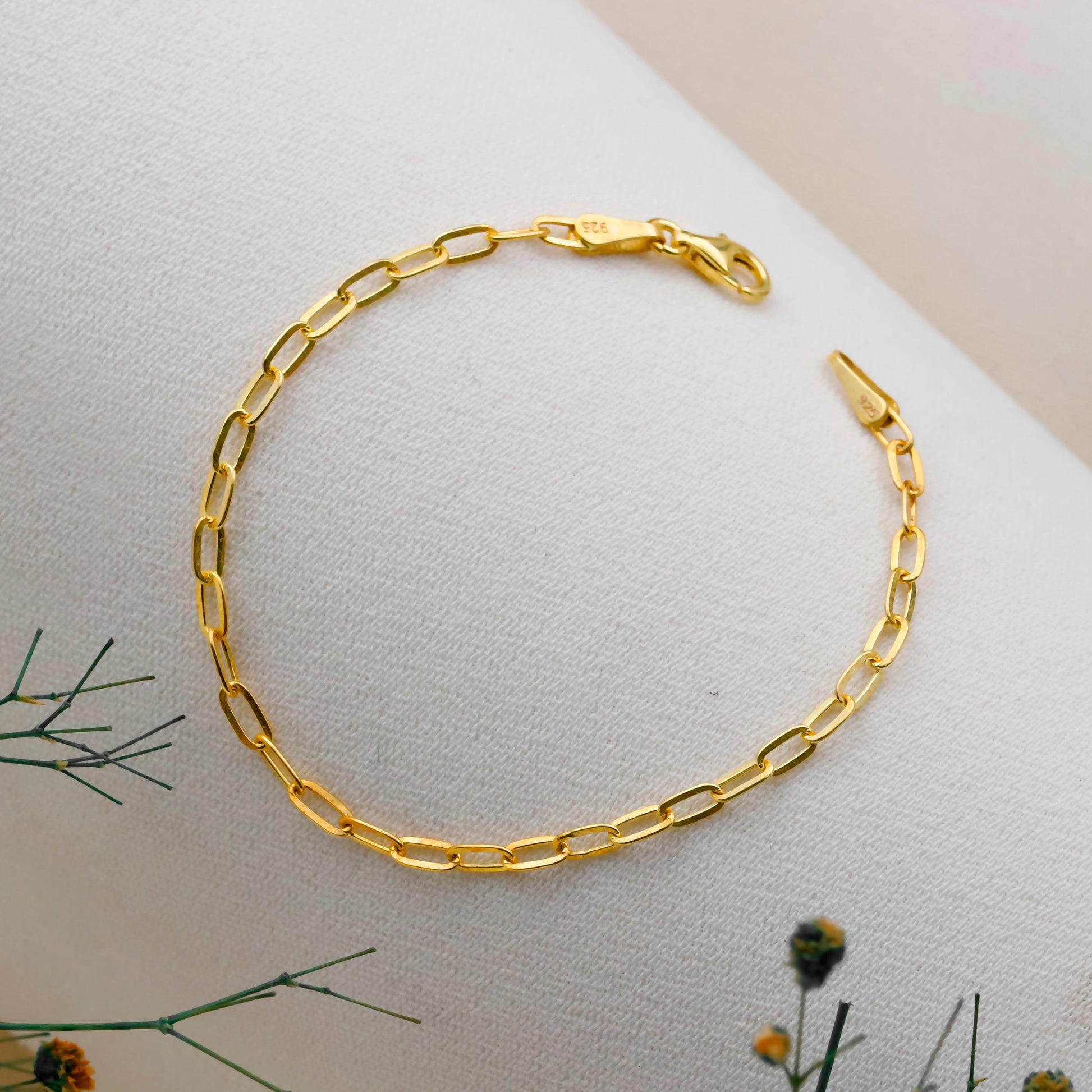 Gold chain bracelet on a light surface with greenery