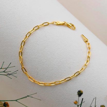Gold chain bracelet on a light surface with greenery