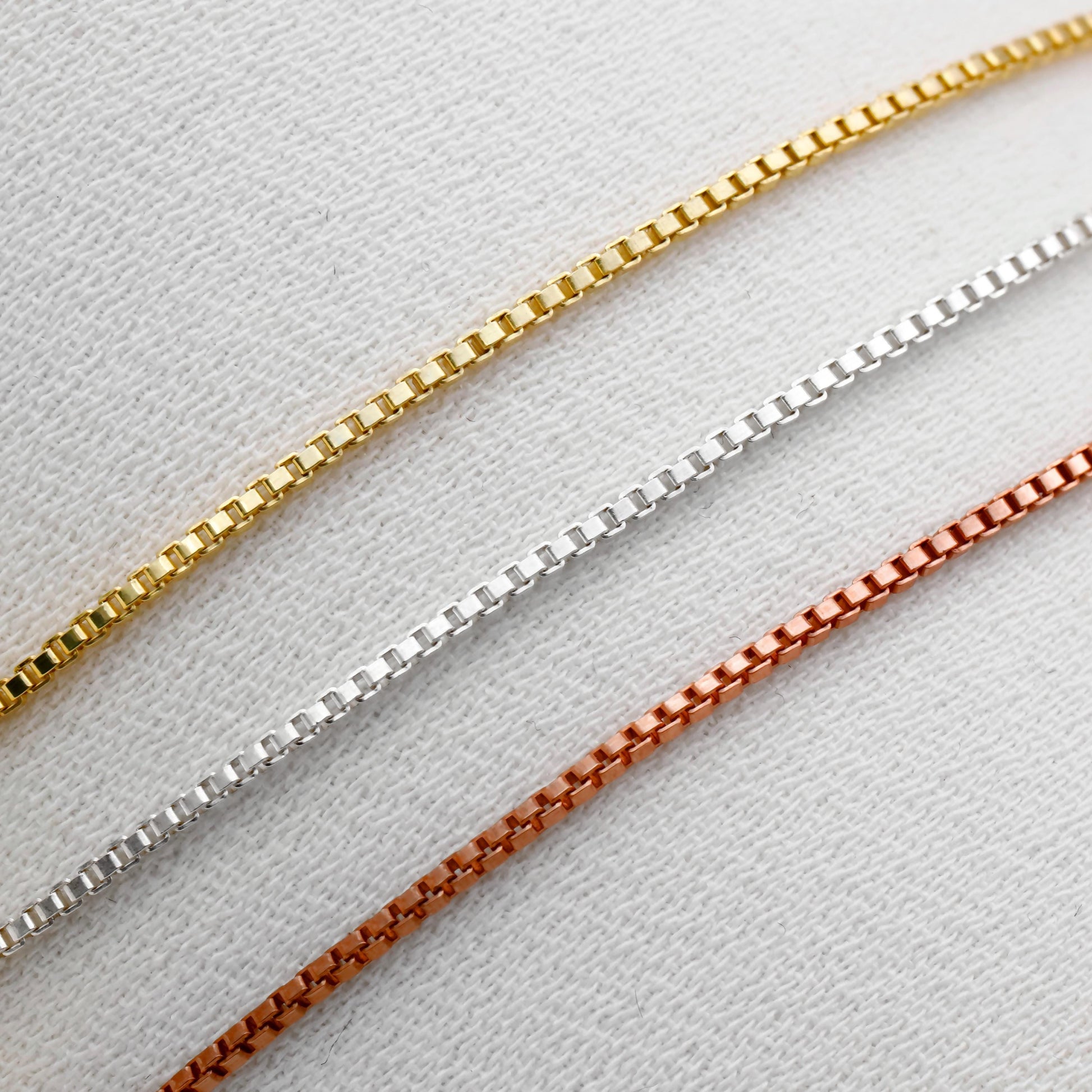 Three gold, silver, and rose gold chain necklaces on a light gray background