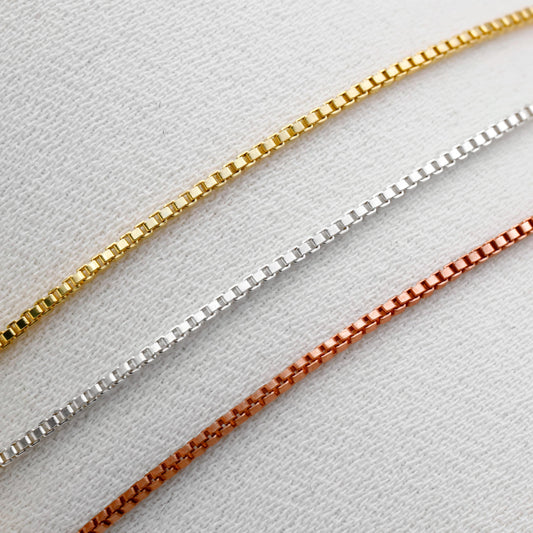 Three gold, silver, and rose gold chain necklaces on a light gray background