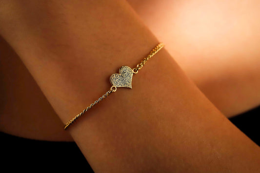 Gold bracelet with a heart-shaped charm on a wrist against a warm background