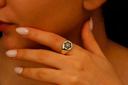 Close-up of a hand wearing a gold ring with a black diamond design.