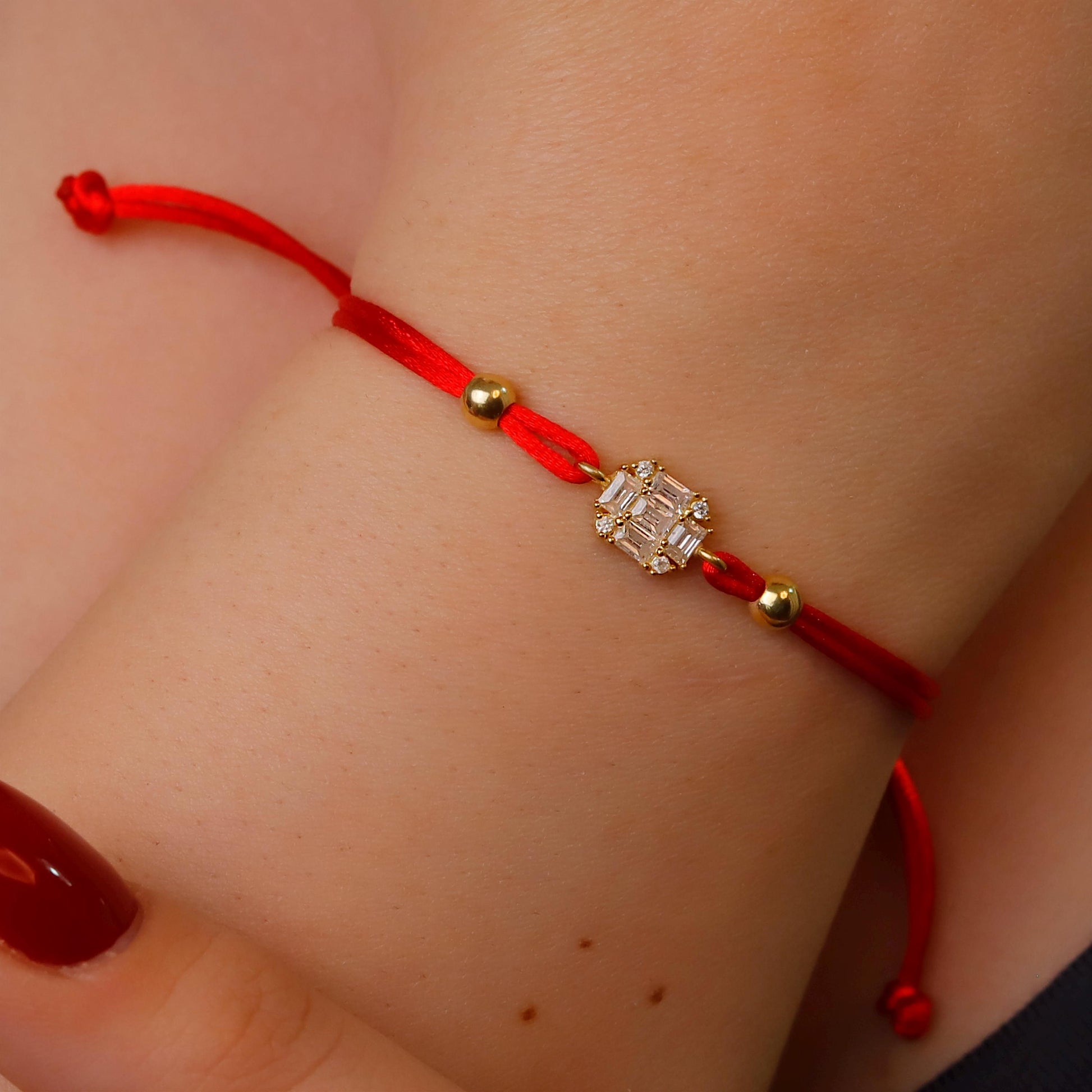 Red string bracelet with a diamond-like charm on a wrist.
