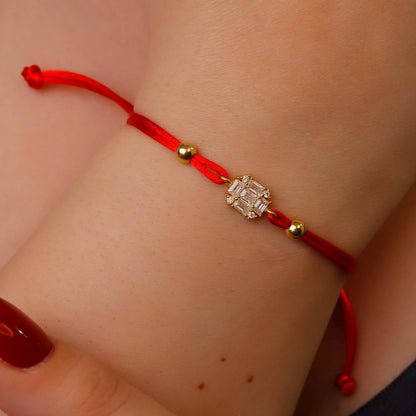 Red string bracelet with a diamond-like charm on a wrist.