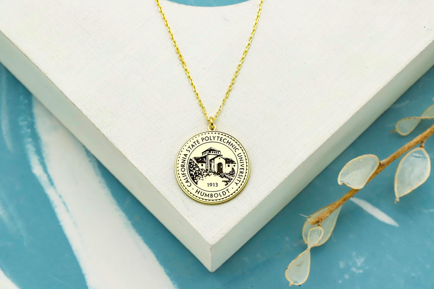 Gold necklace with a round pendant on a white box with a blue base