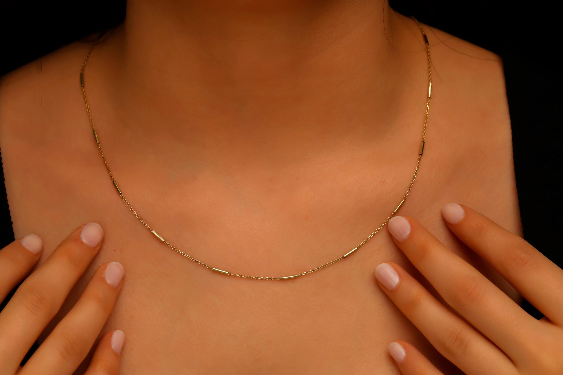 Gold necklace being worn on a person's neck with hands adjusting it against a black background