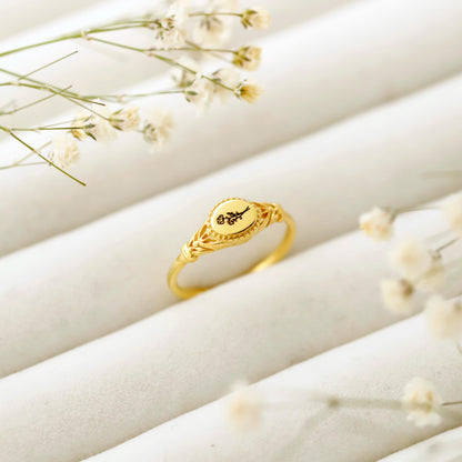 Gold ring with intricate design on a light beige surface with small flowers.