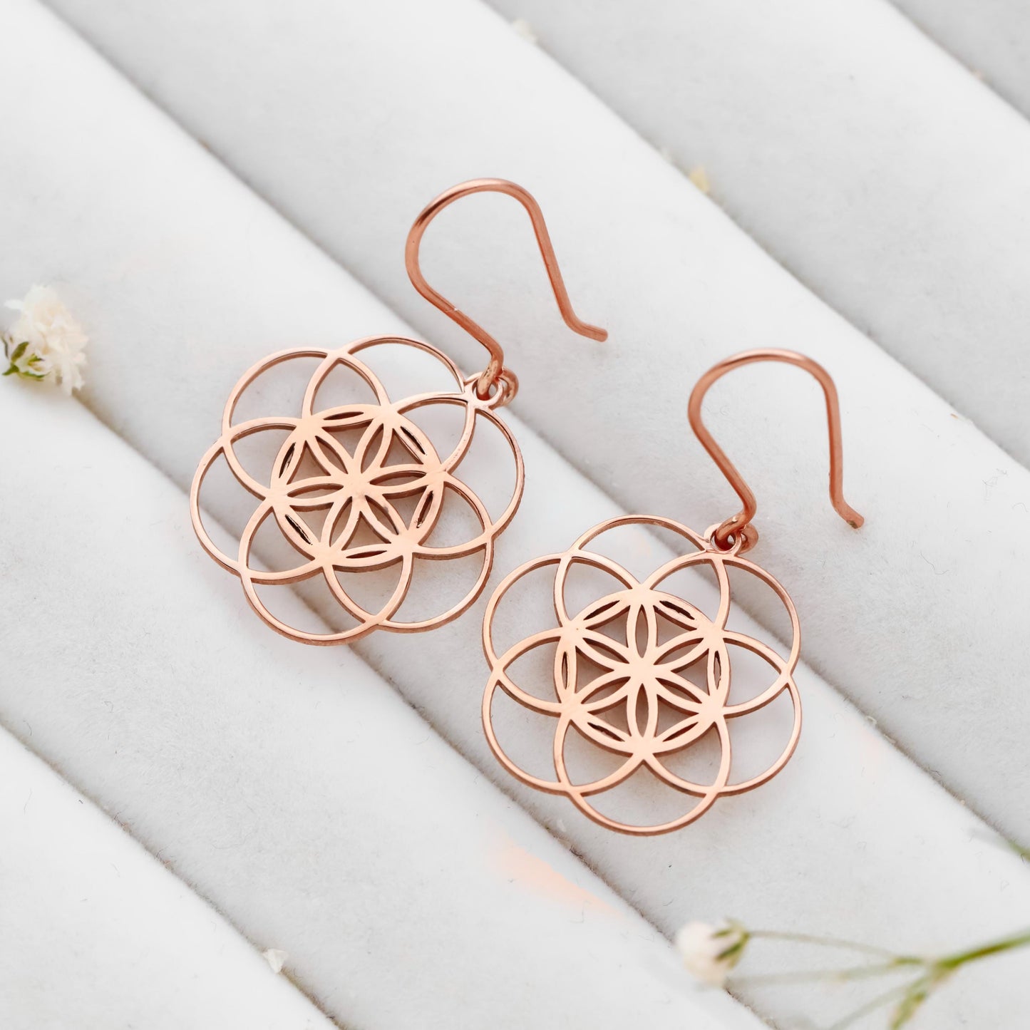 Rose gold floral earrings on a white fabric background