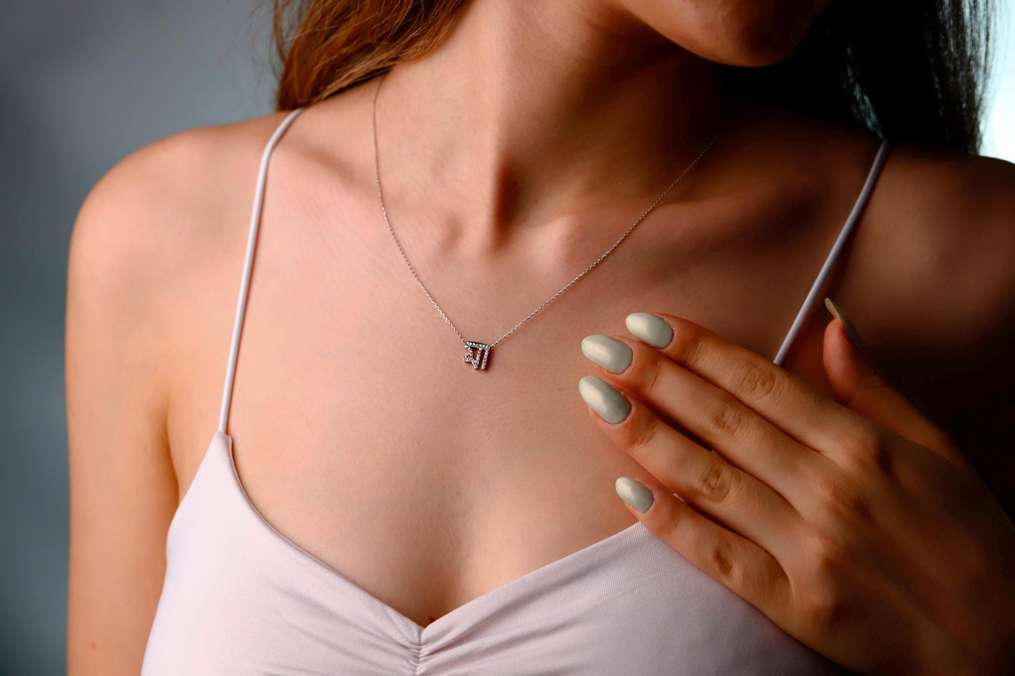 Woman wearing a necklace with a small pendant against a neutral background