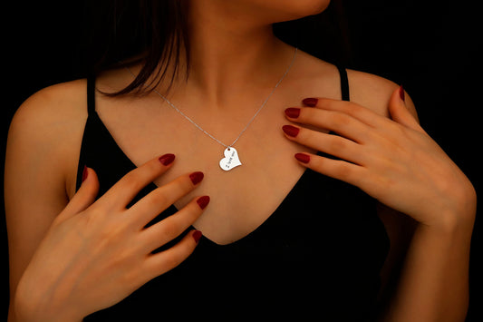 Woman wearing a necklace with a heart-shaped pendant against a dark background