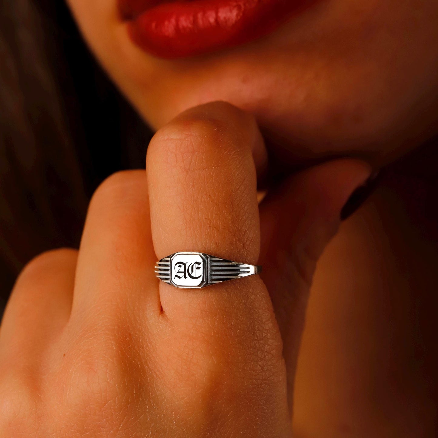 Silver ring with a logo on a person's finger against a warm-toned background