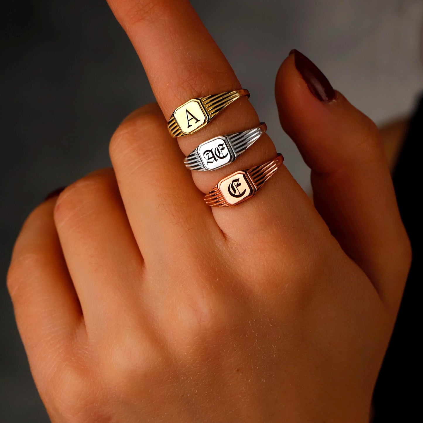 Hand wearing multiple rings with initials on a dark background