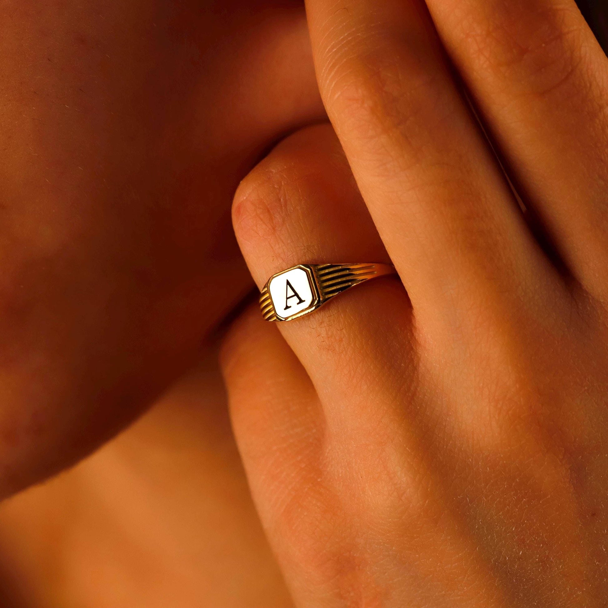 Gold ring with a letter 'A' on a person's finger against a warm-toned background