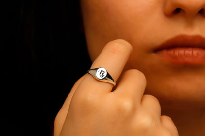 Close-up of a person wearing a ring with a logo on their finger.