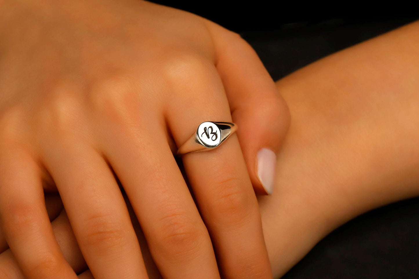 Close-up of a hand wearing a silver ring with a logo on a dark background