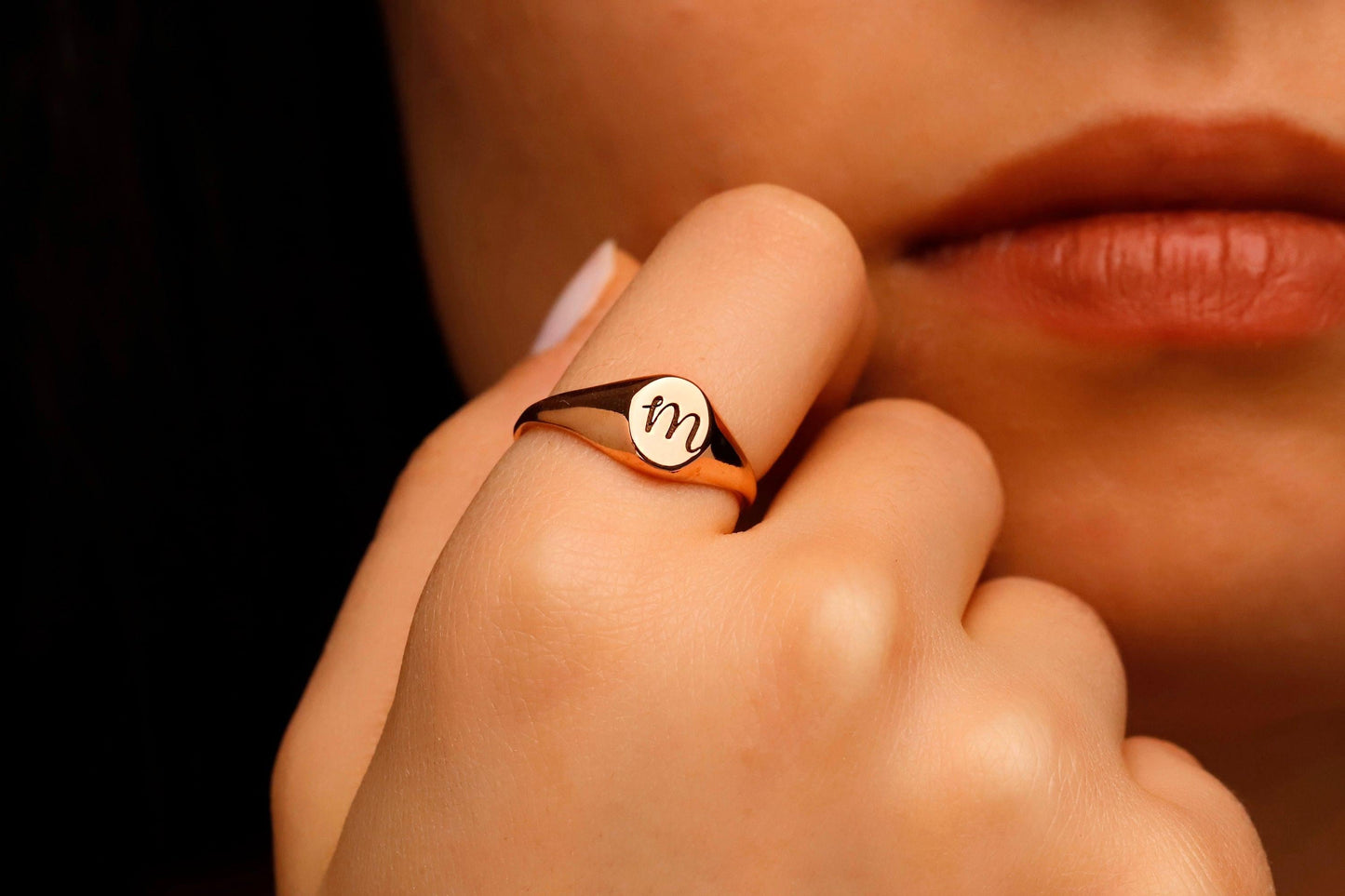 Close-up of a hand wearing a ring with a 'M' symbol, against a blurred background.