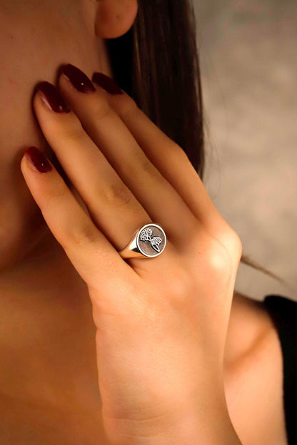 Close-up of a hand wearing a ring with a tree design, against a neutral background.