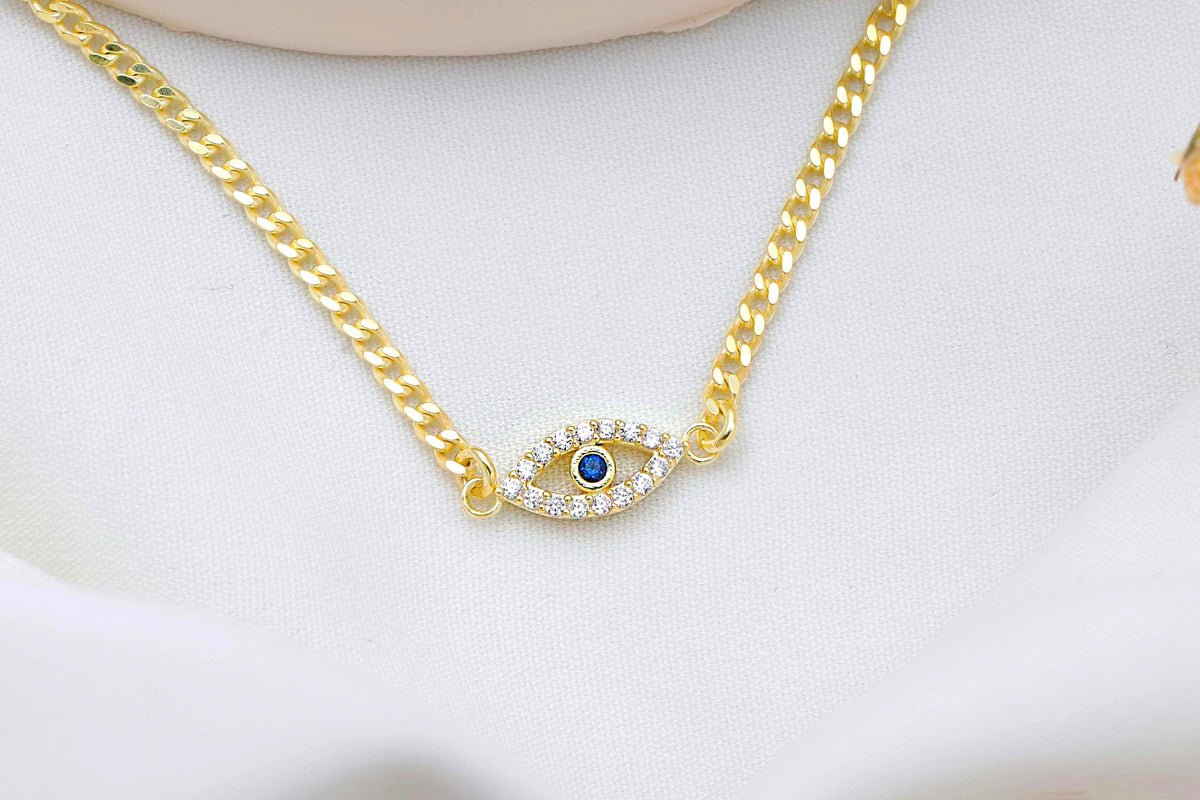 Gold chain necklace with an eye-shaped pendant featuring a blue gemstone on a white background
