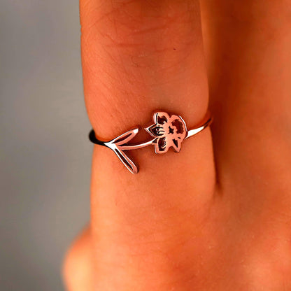 Rose gold ring with a floral design on a person's finger against a neutral background