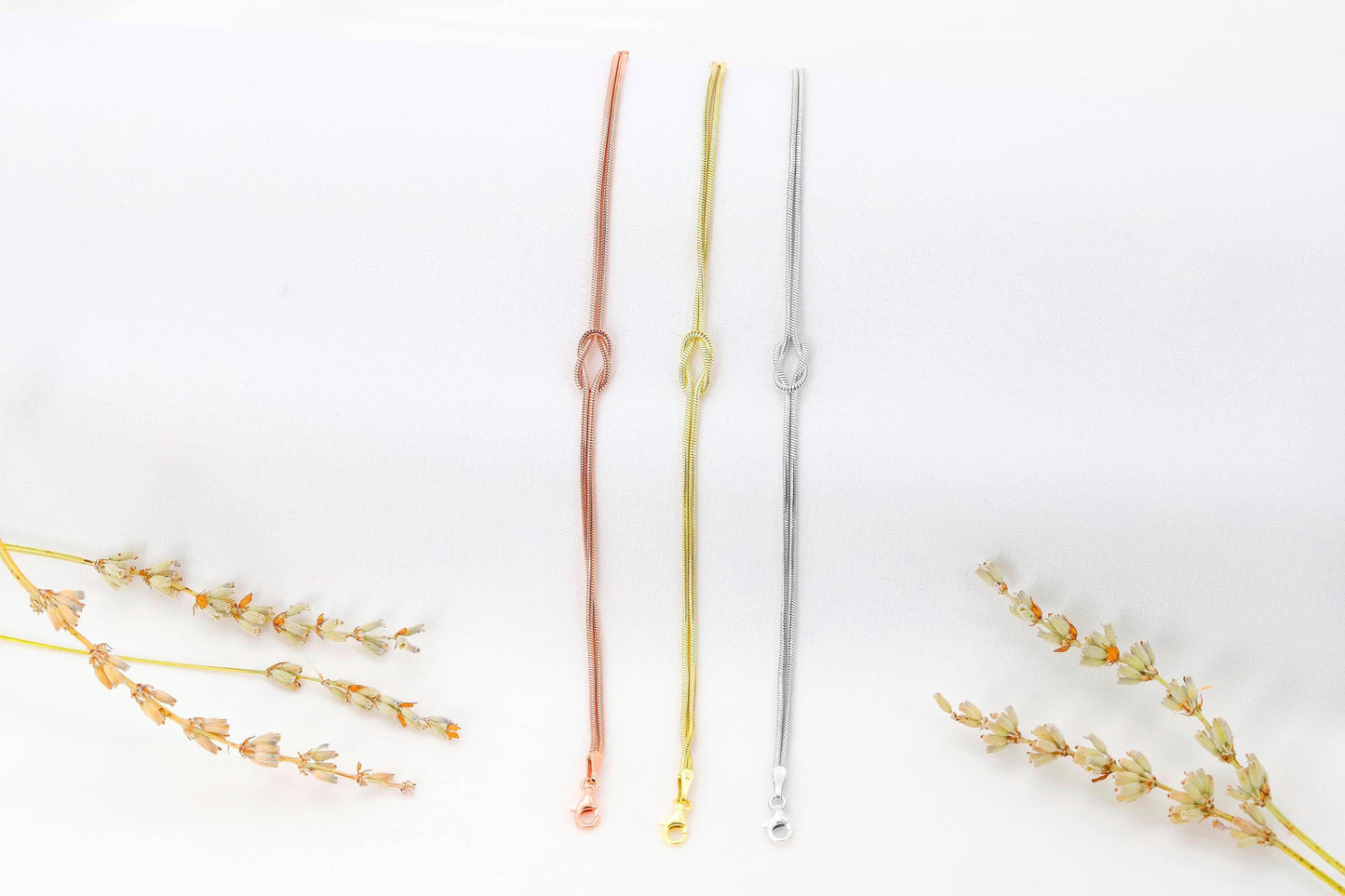 Three gold necklaces on a white background with dried flowers.