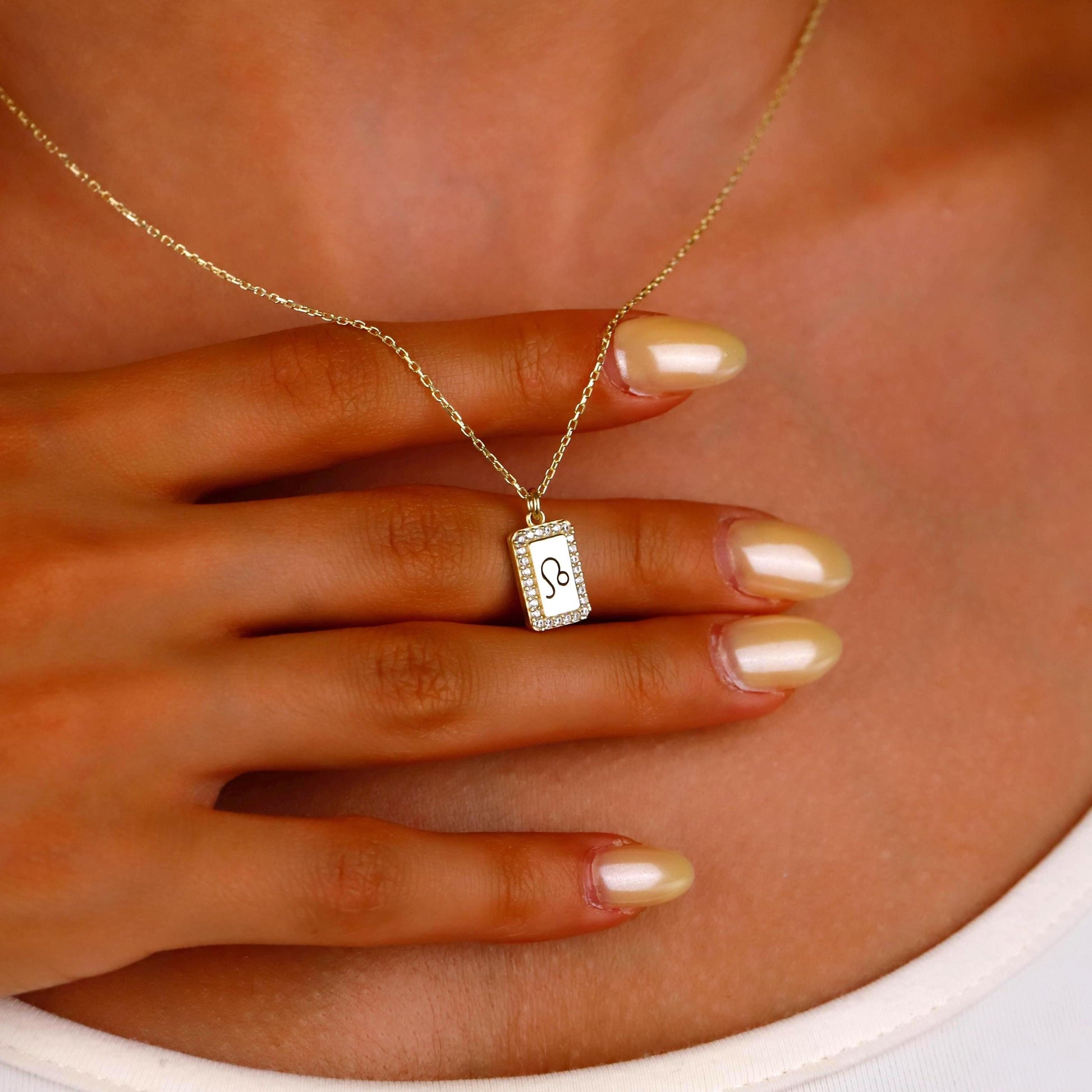 Gold necklace with a pendant on a hand against a neutral background