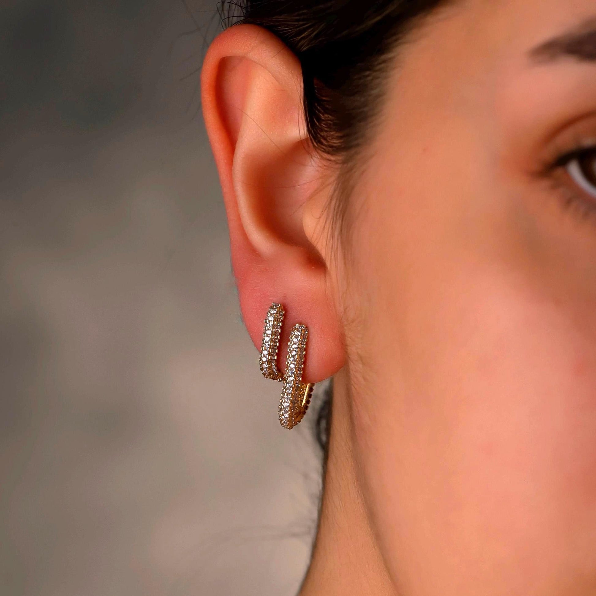 Close-up of a person wearing gold hoop earrings with a blurred background