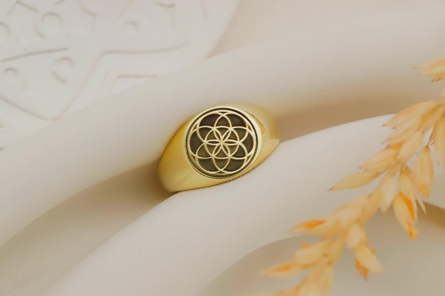 Gold ring with a intricate design on a textured surface with a plant branch.
