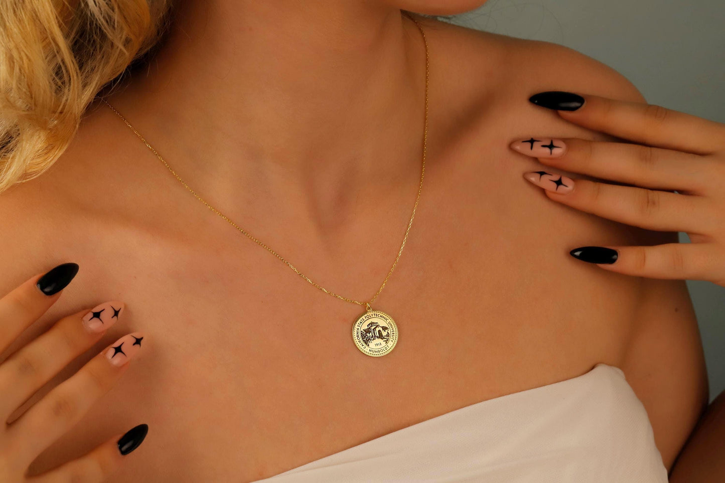 Gold necklace with a pendant worn by a person with black nail polish.